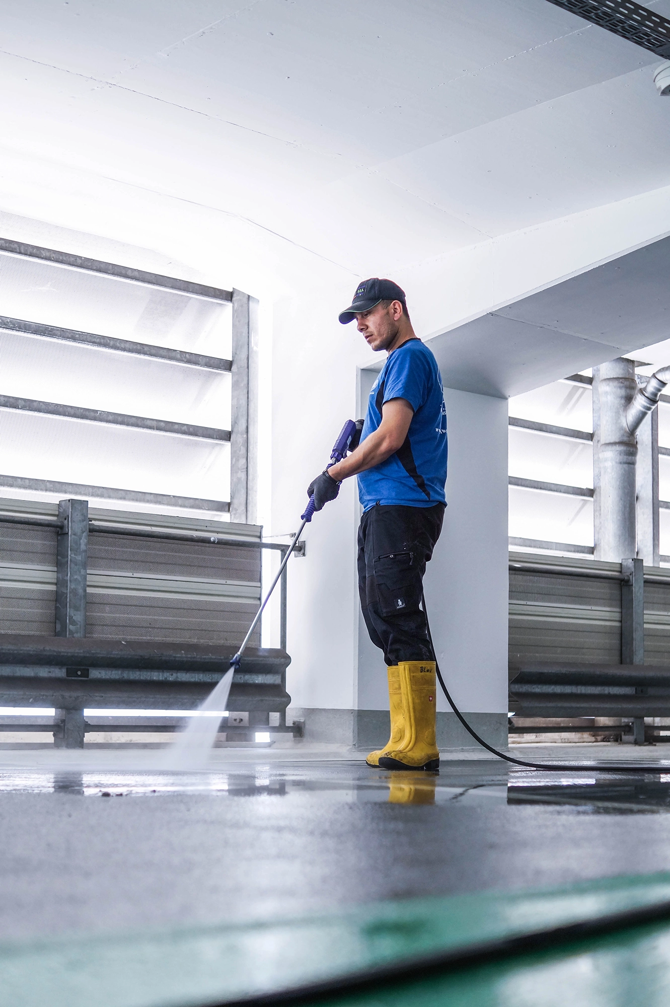 Das Bild zeigt einen Mitarbeiter der Firma Albo-Service, der den Boden eines Parkhauses mit einem Hochdruckreiniger reinigt.
